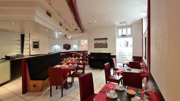 Un restaurante moderno con decoración en rojo y negro, varias mesas de comedor y un piano en el centro.