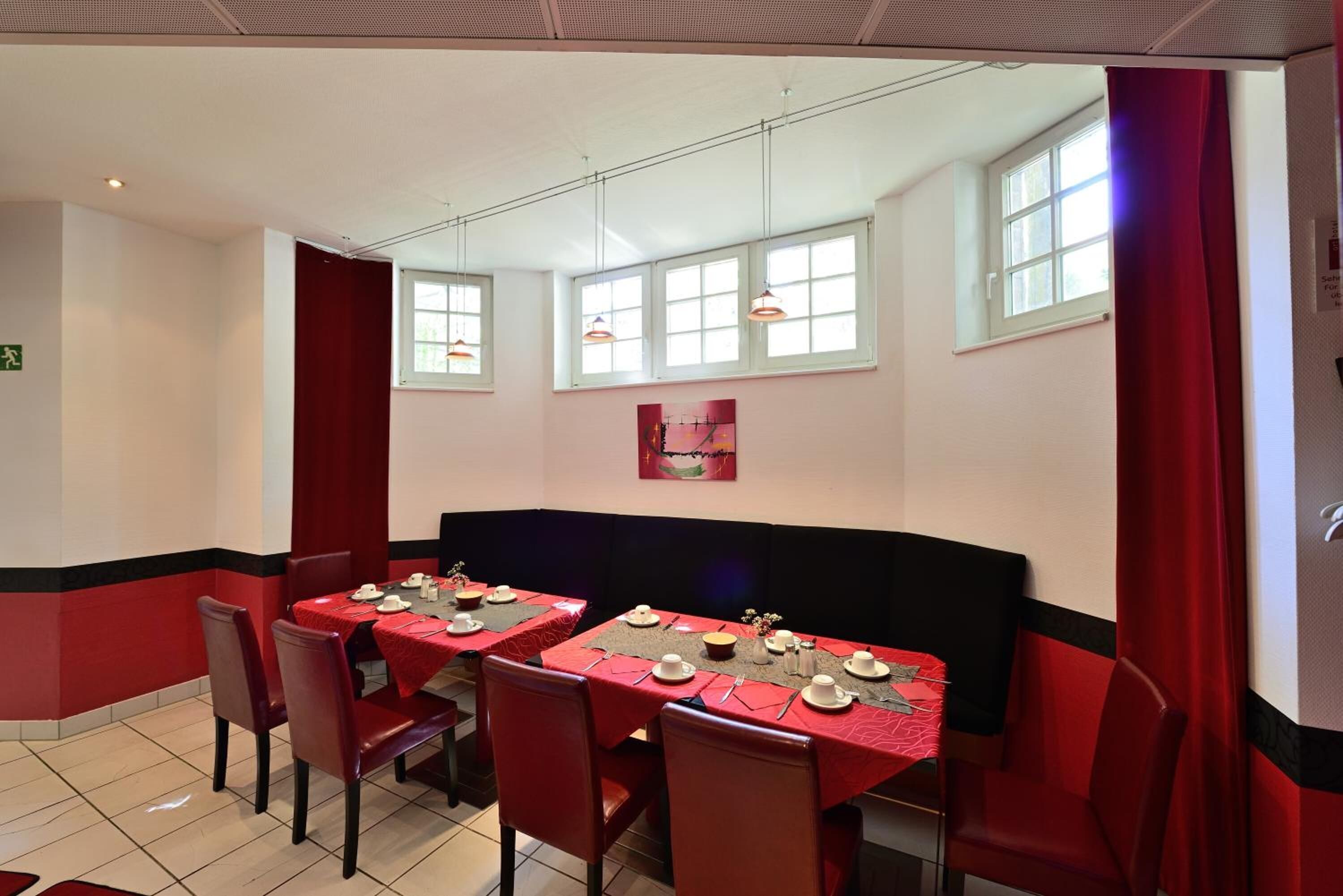 Un restaurante con decoración roja y negra, varias mesas dispuestas para comer y grandes ventanales.