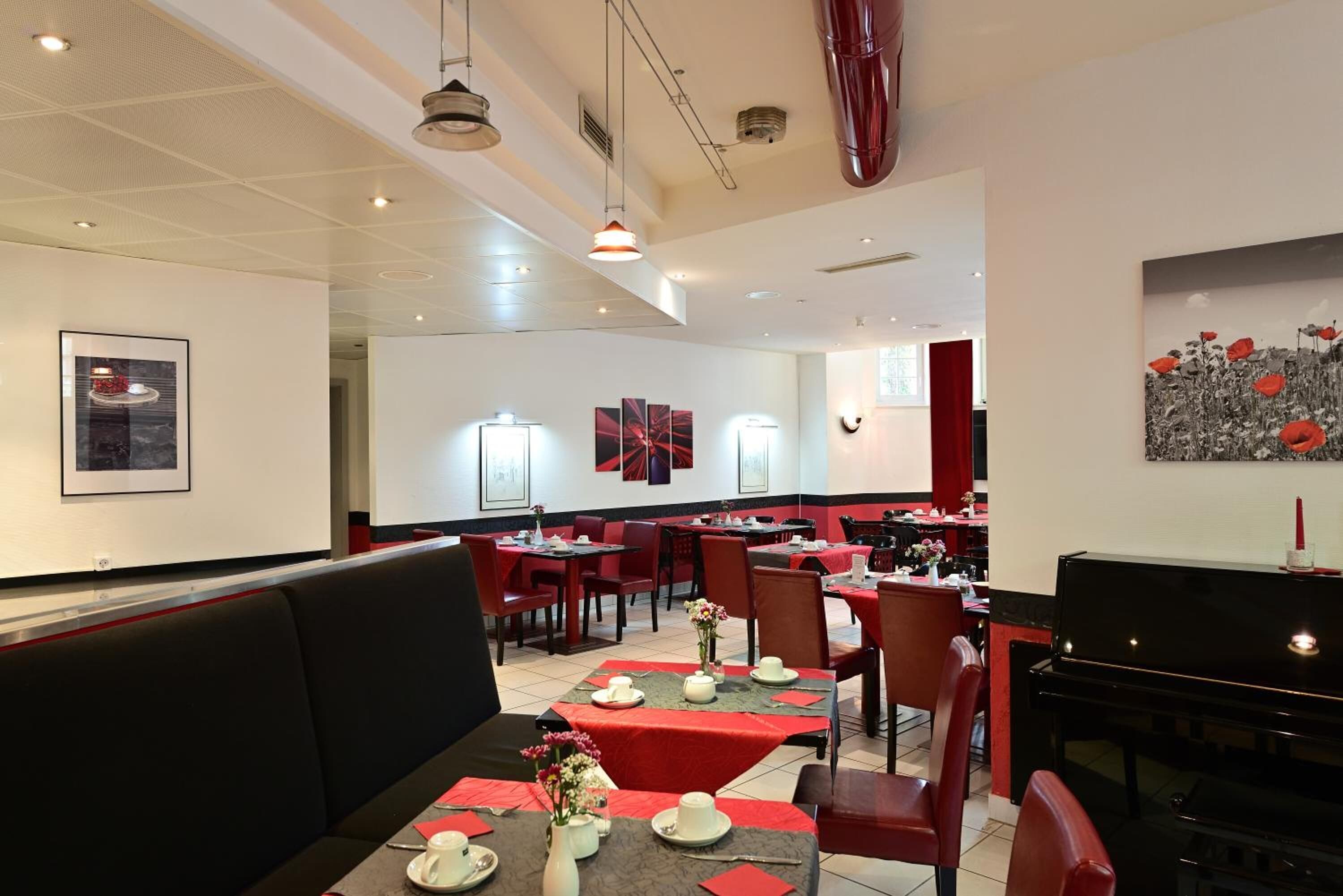 A restaurant with booths and tables, red and black decor, and a piano.