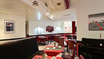 A restaurant with booths and tables, red and black decor, and a piano.