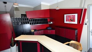A compact kitchen with red and black cabinetry, a wooden countertop, and a hanging light fixture. - Art Hotel Weimar (Weimar)