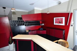 Una cocina compacta con armarios rojo y negro, una encimera de madera y una lámpara colgante.