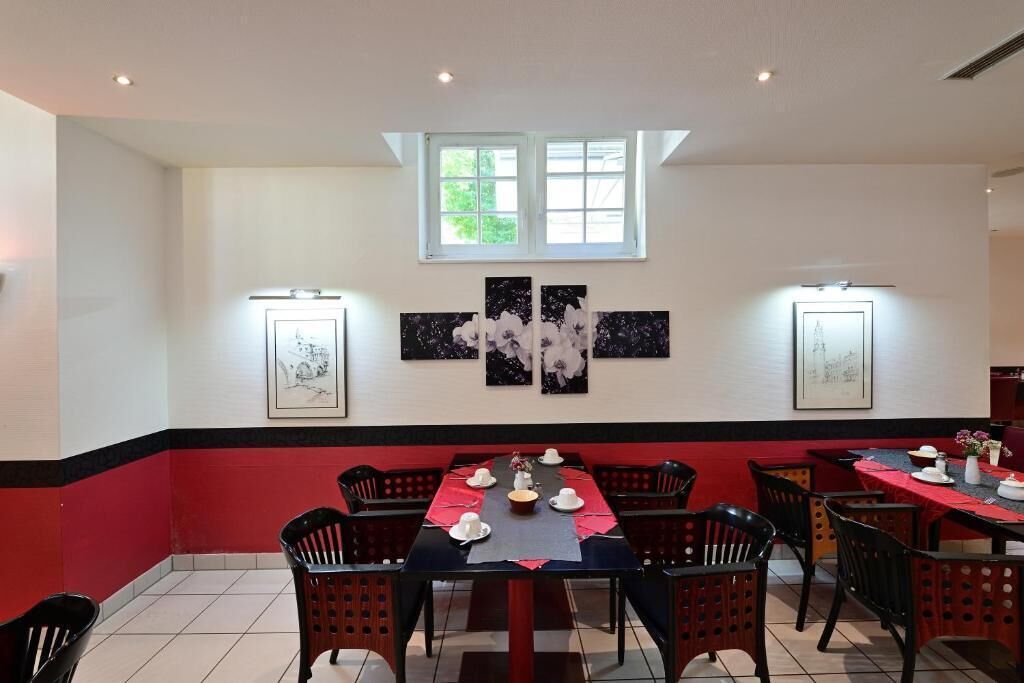 A dining area with tables set for a meal, chairs, artwork on the walls, and a window providing natural light.