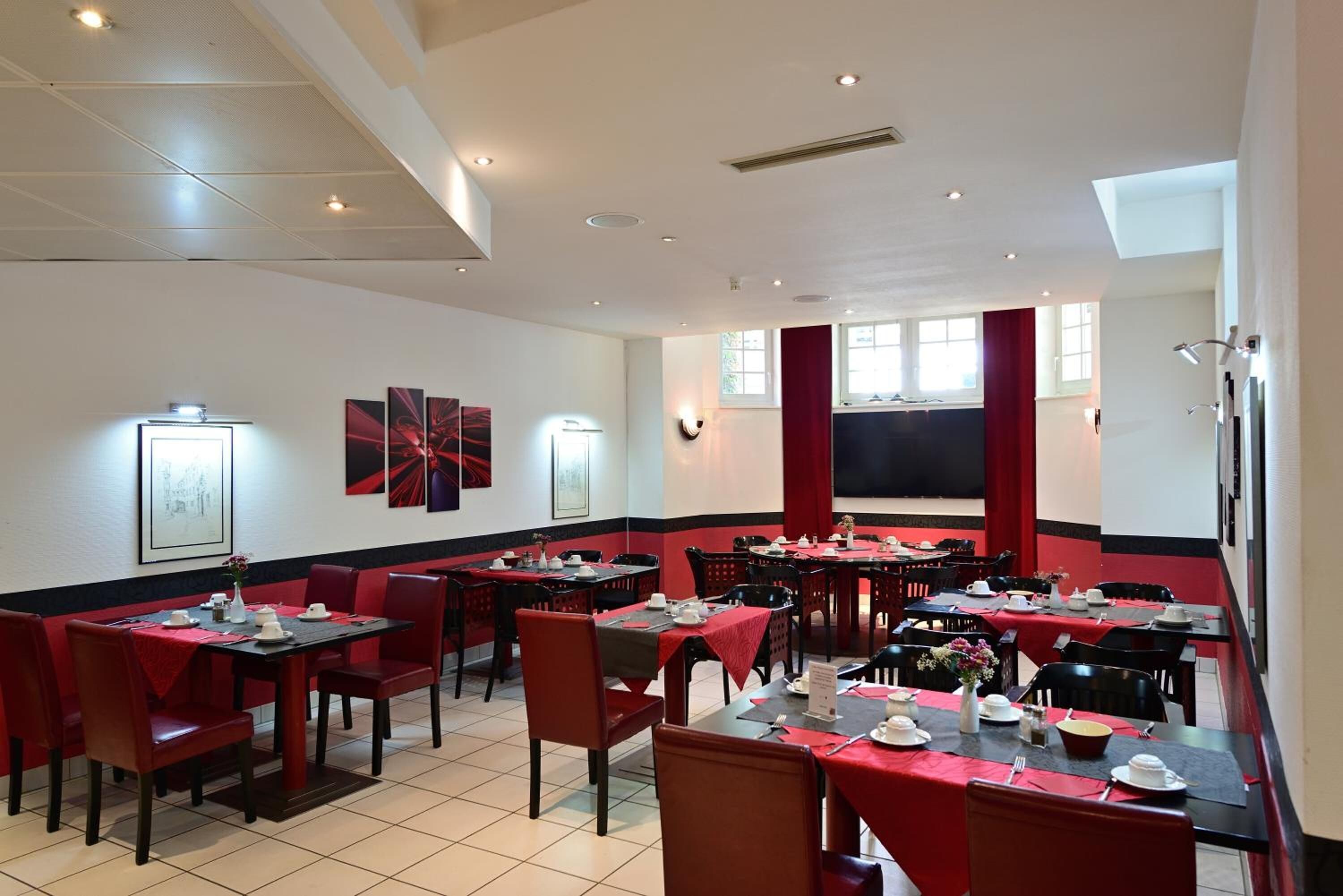 Een restaurant met rode en zwarte decoratie, meerdere tafels en stoelen.