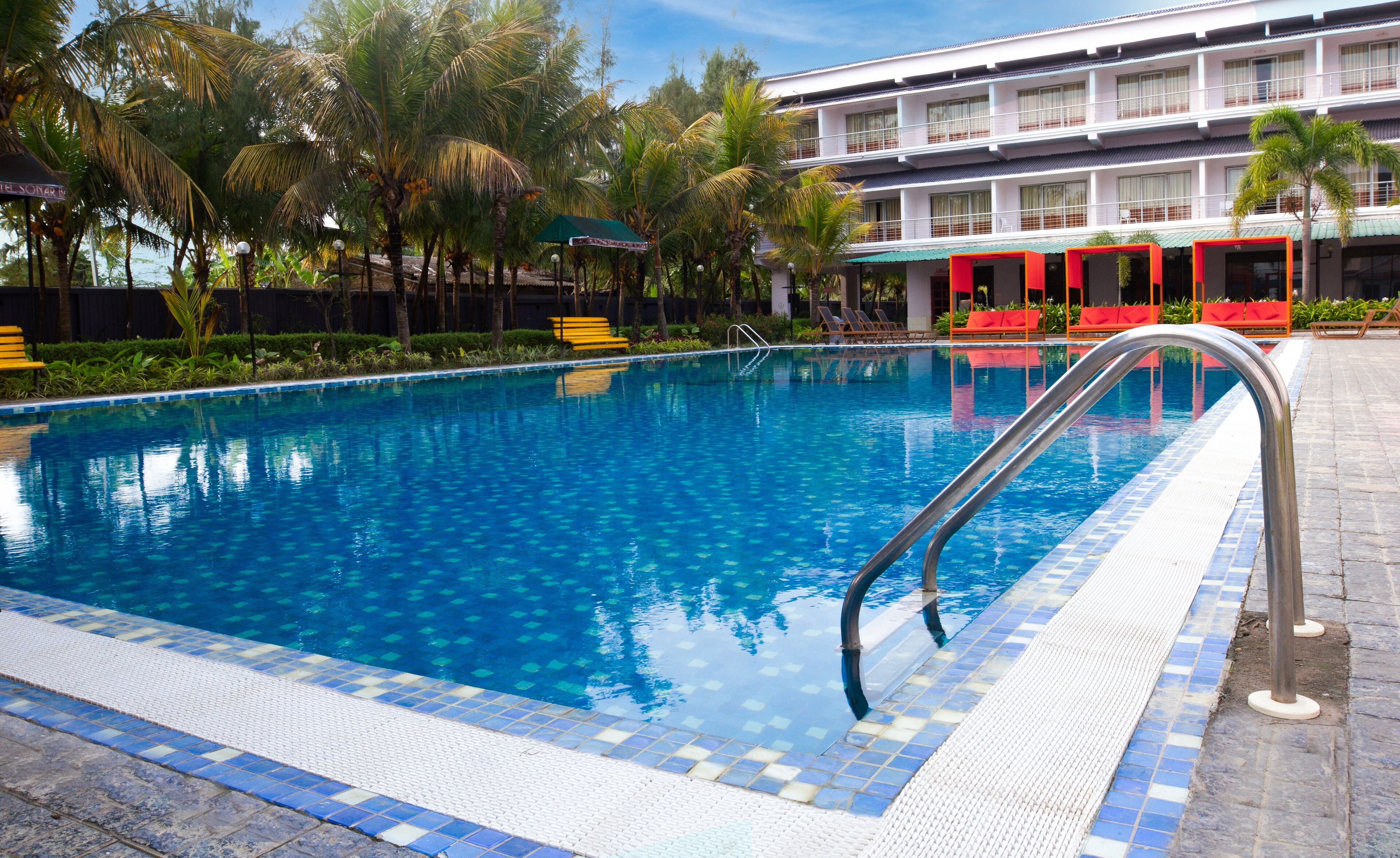 A swimming pool with clear blue water, surrounded by palm trees and a building with balconies.