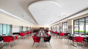 Un vaste espace dédié à la salle à manger, avec de nombreuses tables et chaises, de grandes fenêtres et des ventilateurs de plafond.