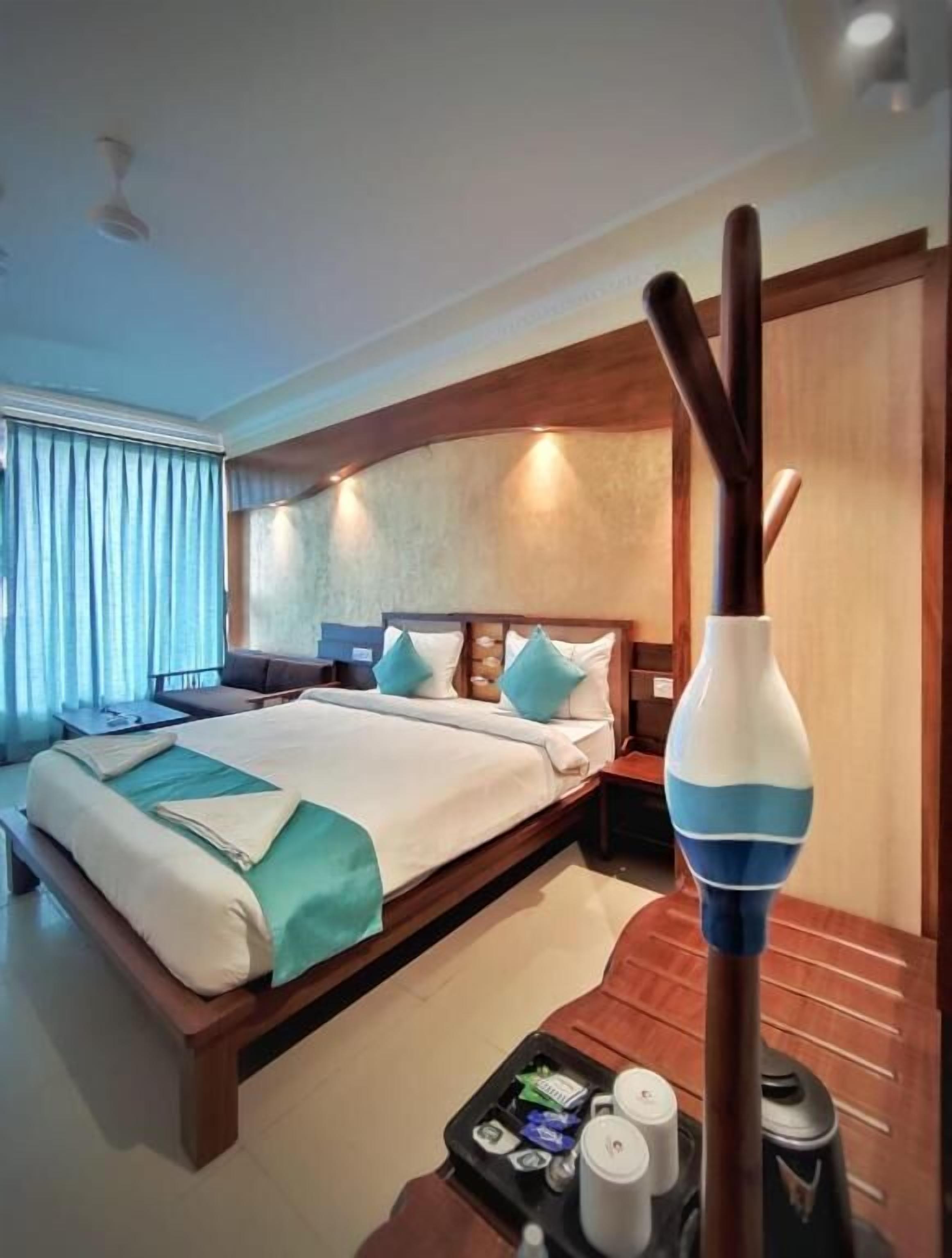 Una habitación de hotel con una cama grande, cabecera de madera y una mesita de noche con lámpara.