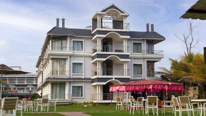 Un hôtel à plusieurs étages, doté de balcons, de sièges en plein air et d’un parasol rouge.