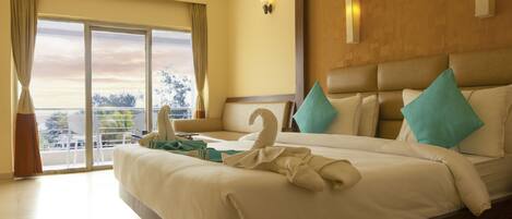 A hotel room with a large bed, a balcony with a view, and a ceiling fan.
