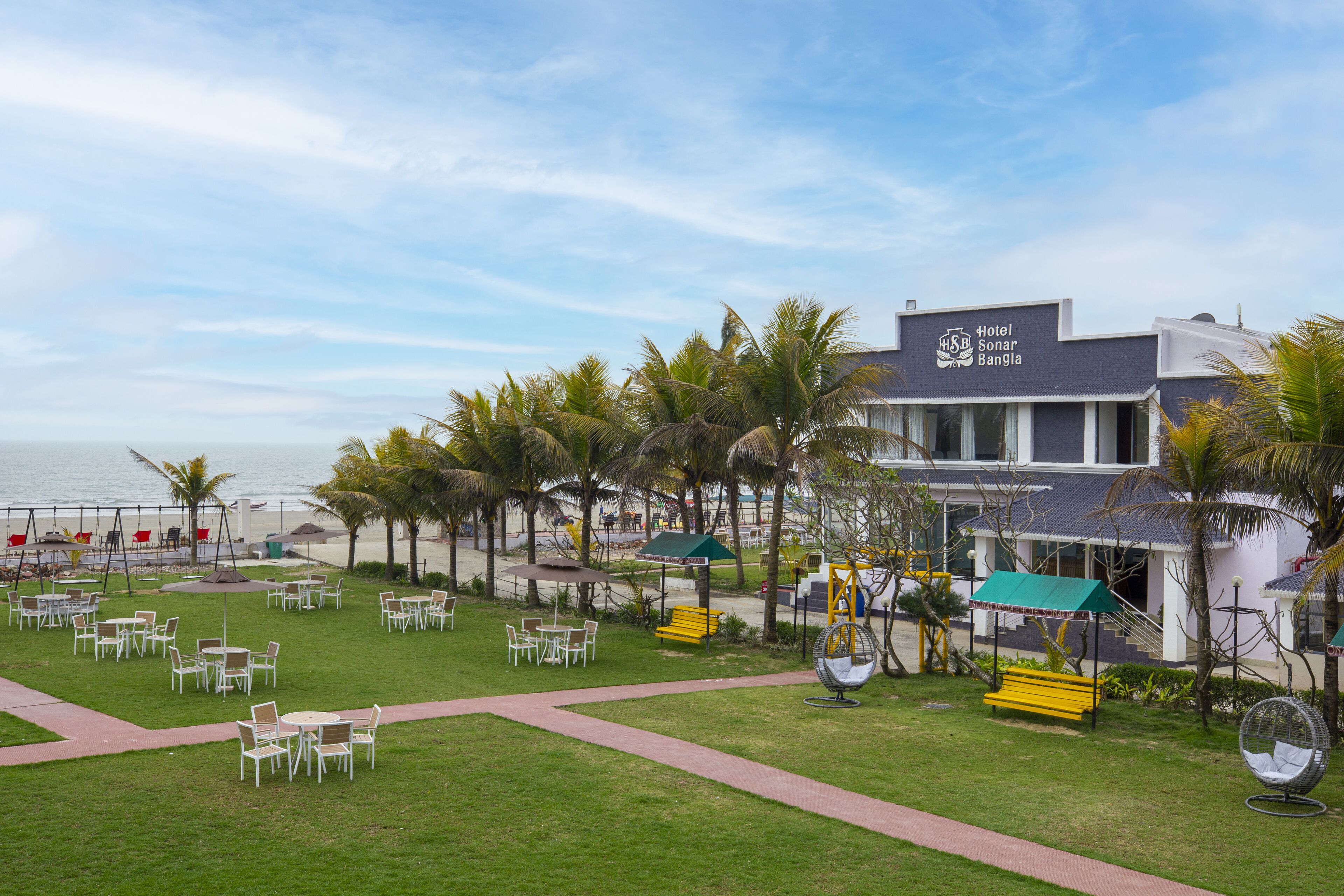 A hotel with a beach view, outdoor seating, and palm trees.