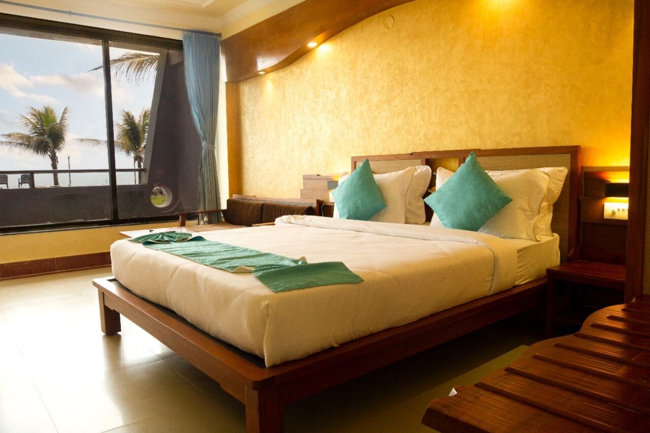 A hotel room with a large bed, wooden headboard, and a view of palm trees through a window.