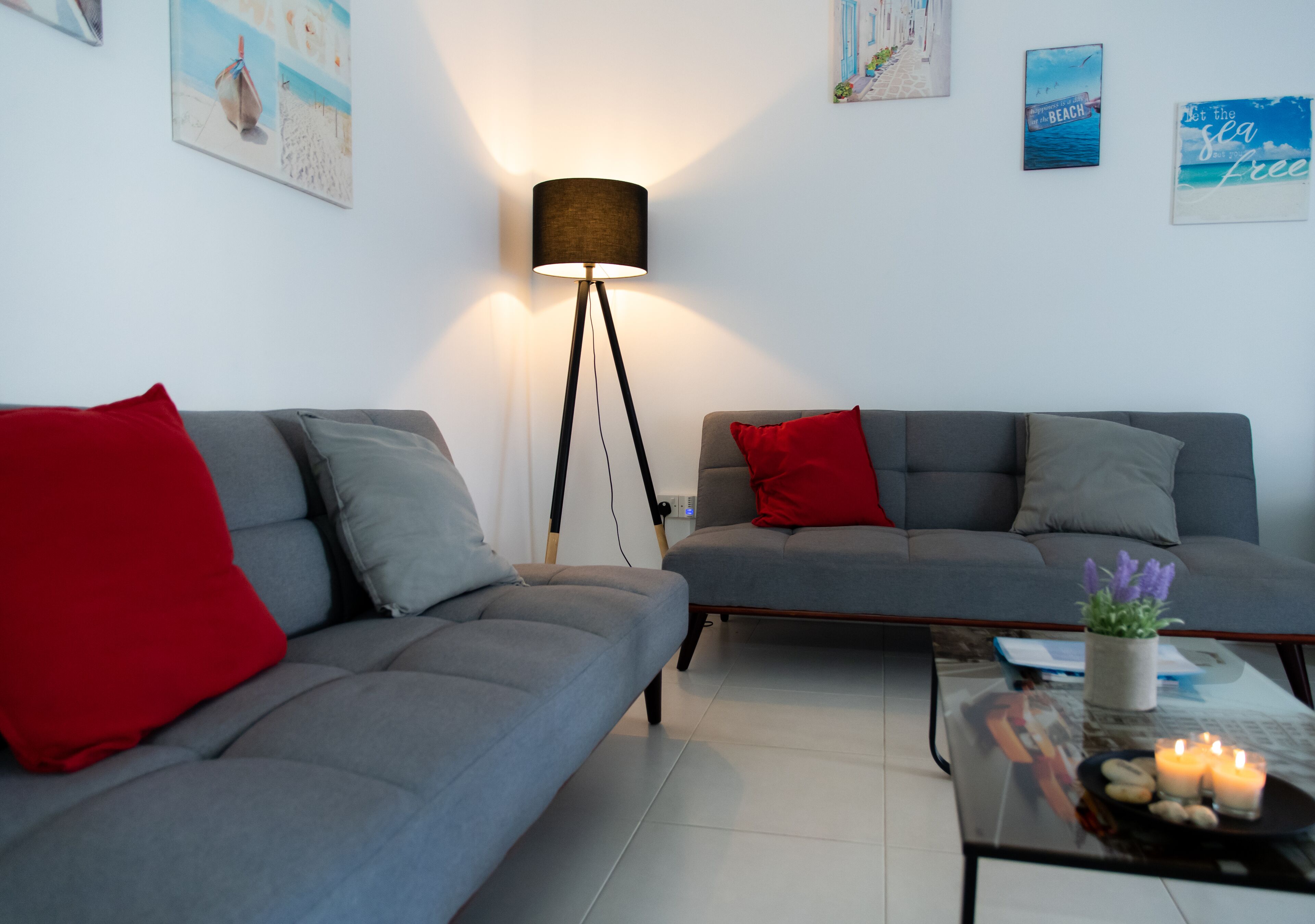 A modern living room with two grey sofas, one with a red pillow, a floor lamp, and a coffee table with a candle and a plant.