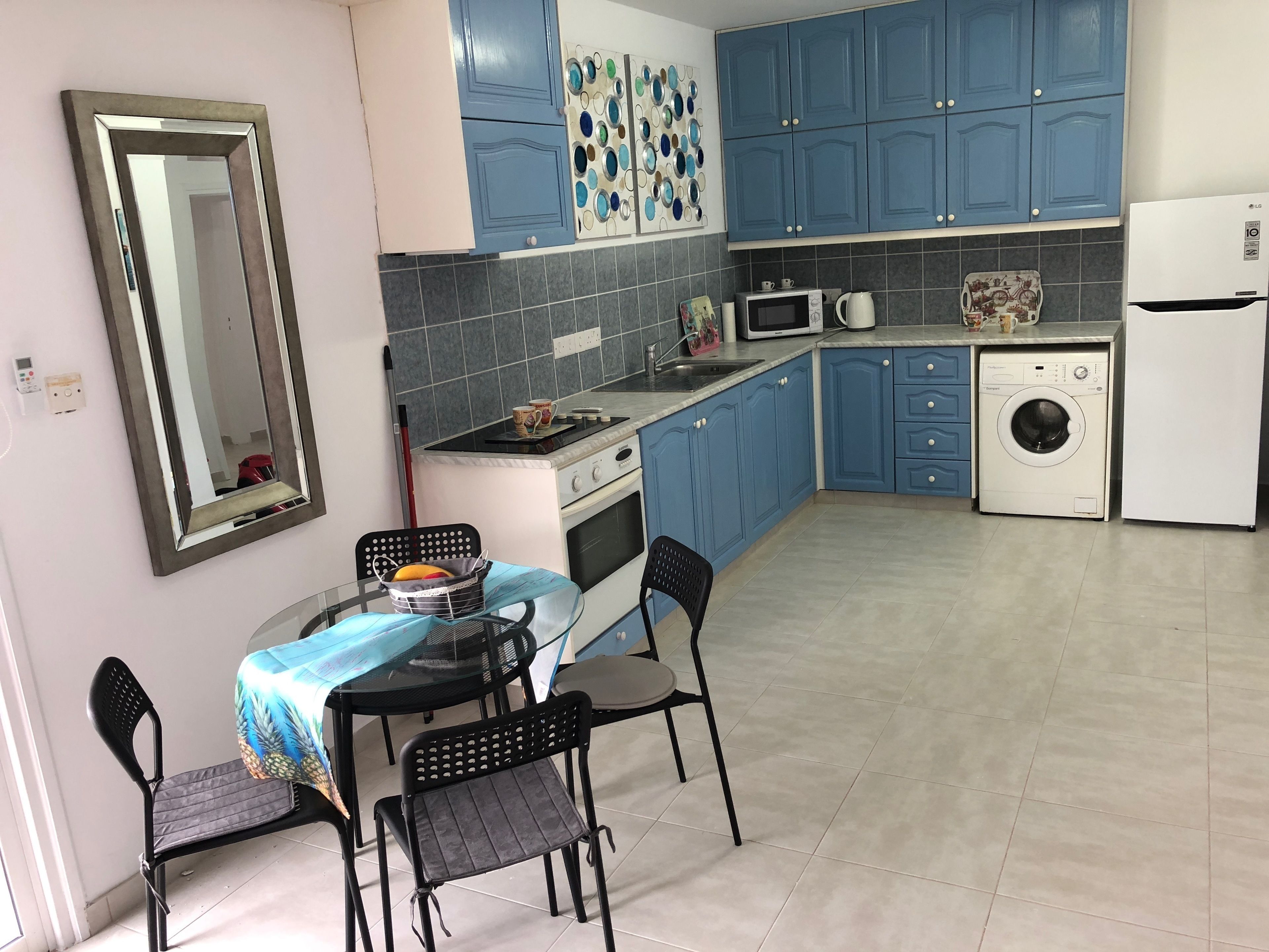Cocina compacta con armarios azules, microondas, lavadora y comedor con mesa y sillas.