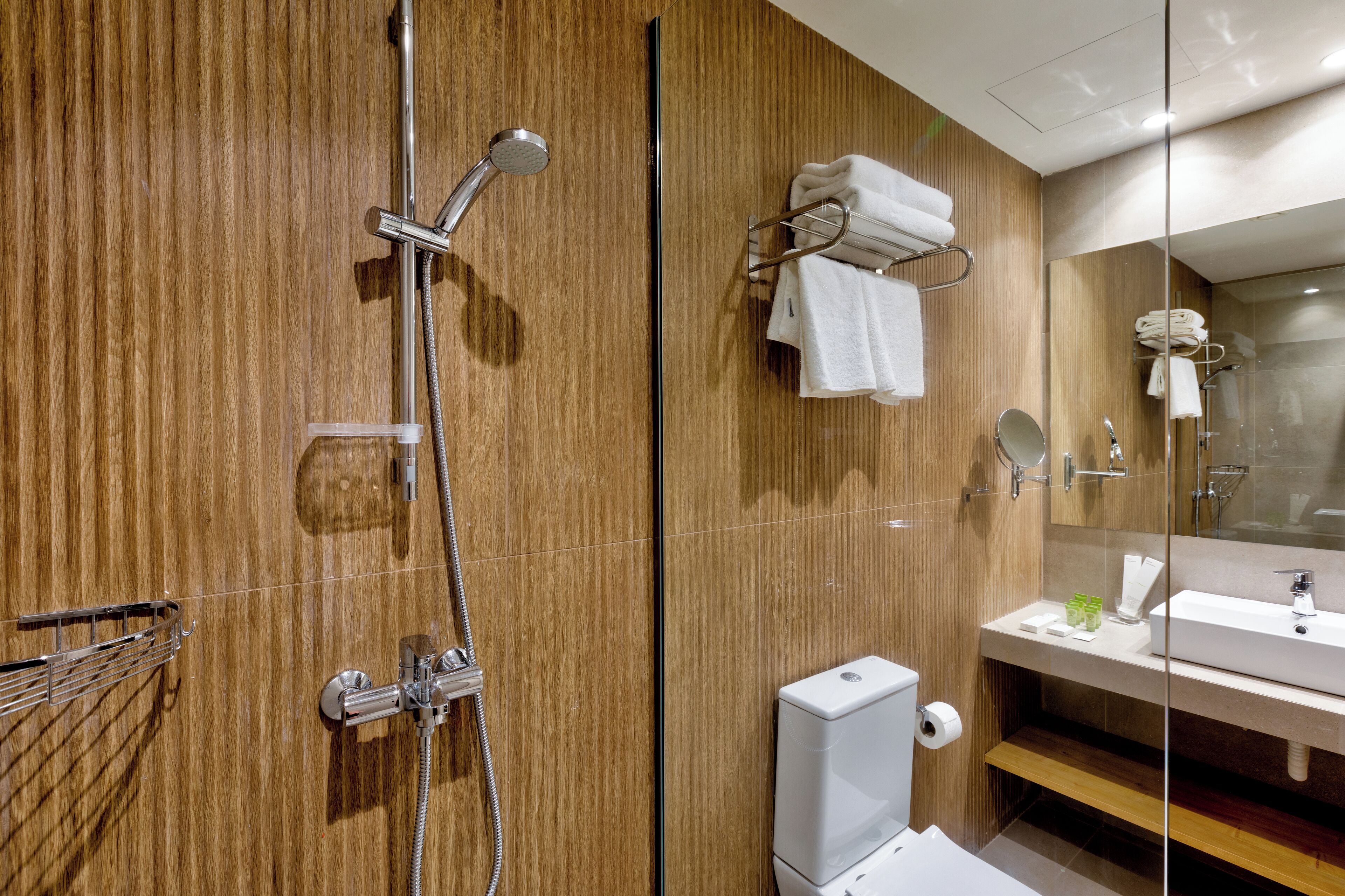 A modern bathroom with a wooden wall, a glass shower enclosure, a white sink, and a towel rack.