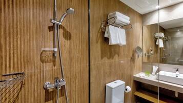 A modern bathroom with a wooden wall, a glass shower enclosure, a white sink, and a towel rack.