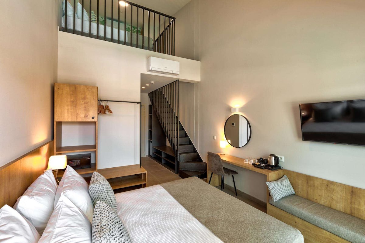 A hotel room with a bed, a desk, a chair, a TV, a staircase, and a small balcony.
