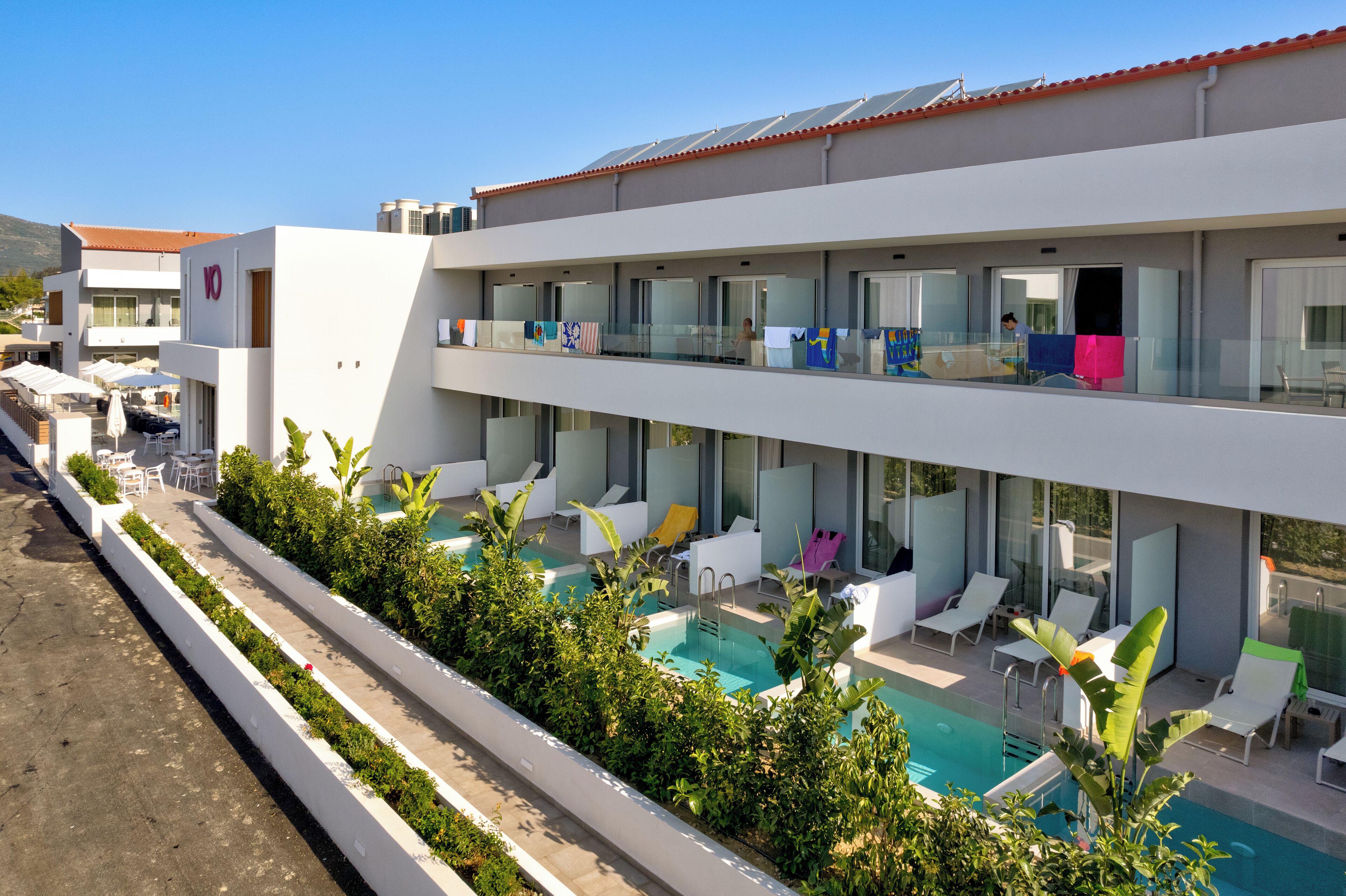 Un hotel moderno con piscina en la azotea, varios balcones y zonas de estar al aire libre.