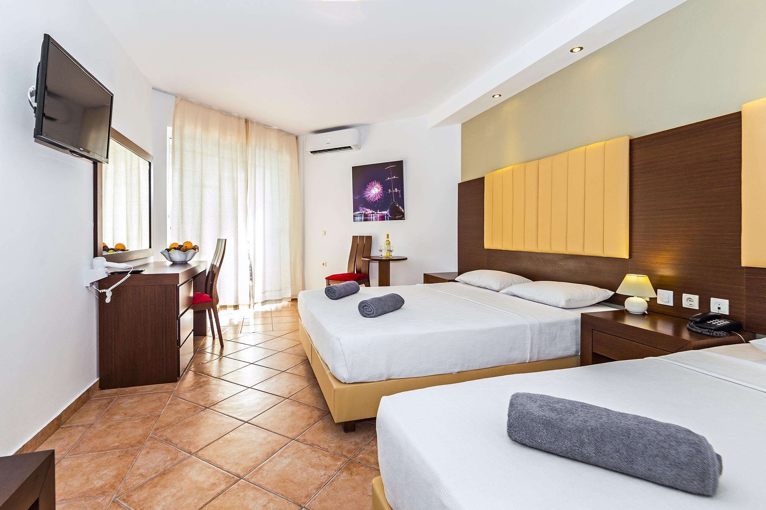 A hotel room with two beds, a desk with a chair, a TV, and a window with curtains.
