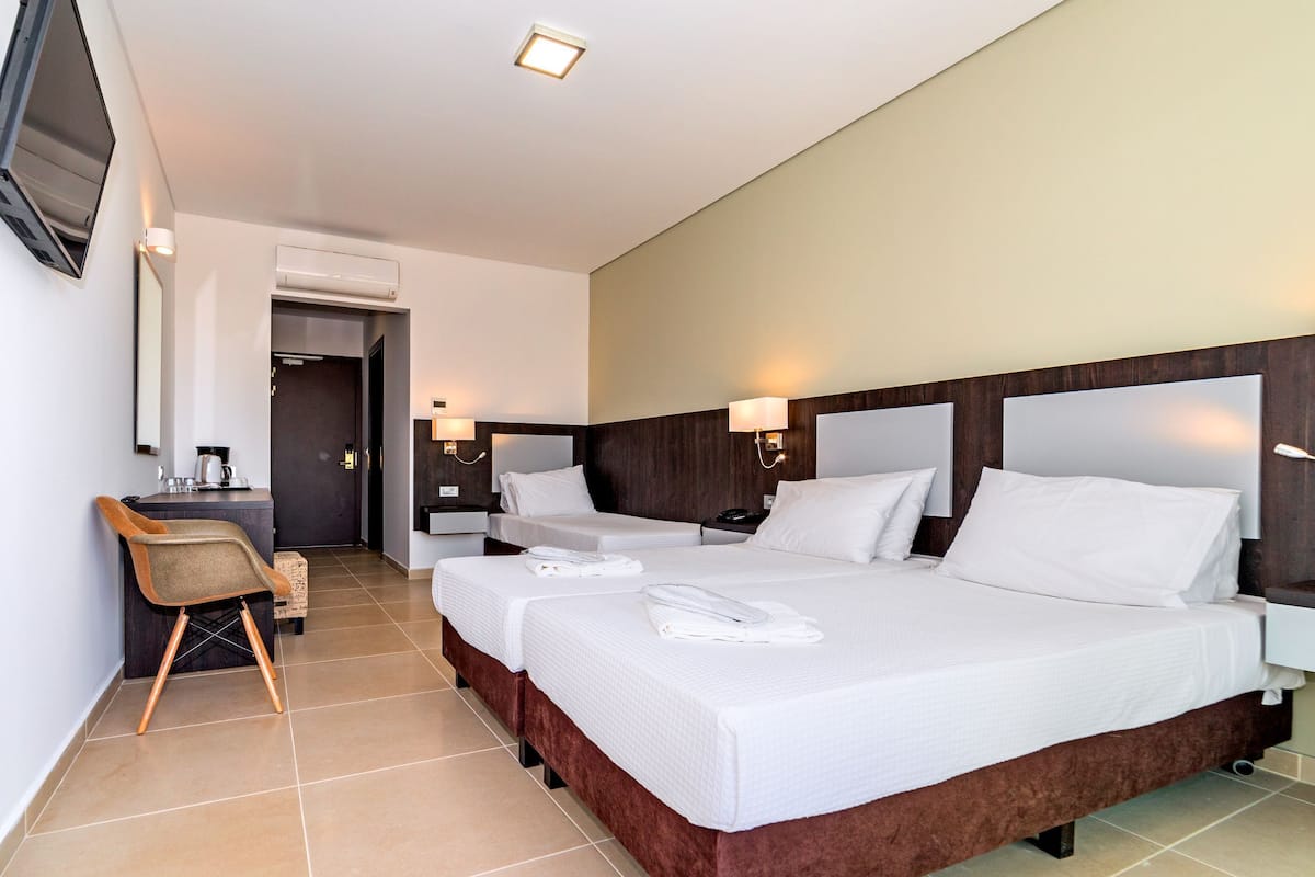 A hotel room with two beds, a desk, a chair, and a TV.