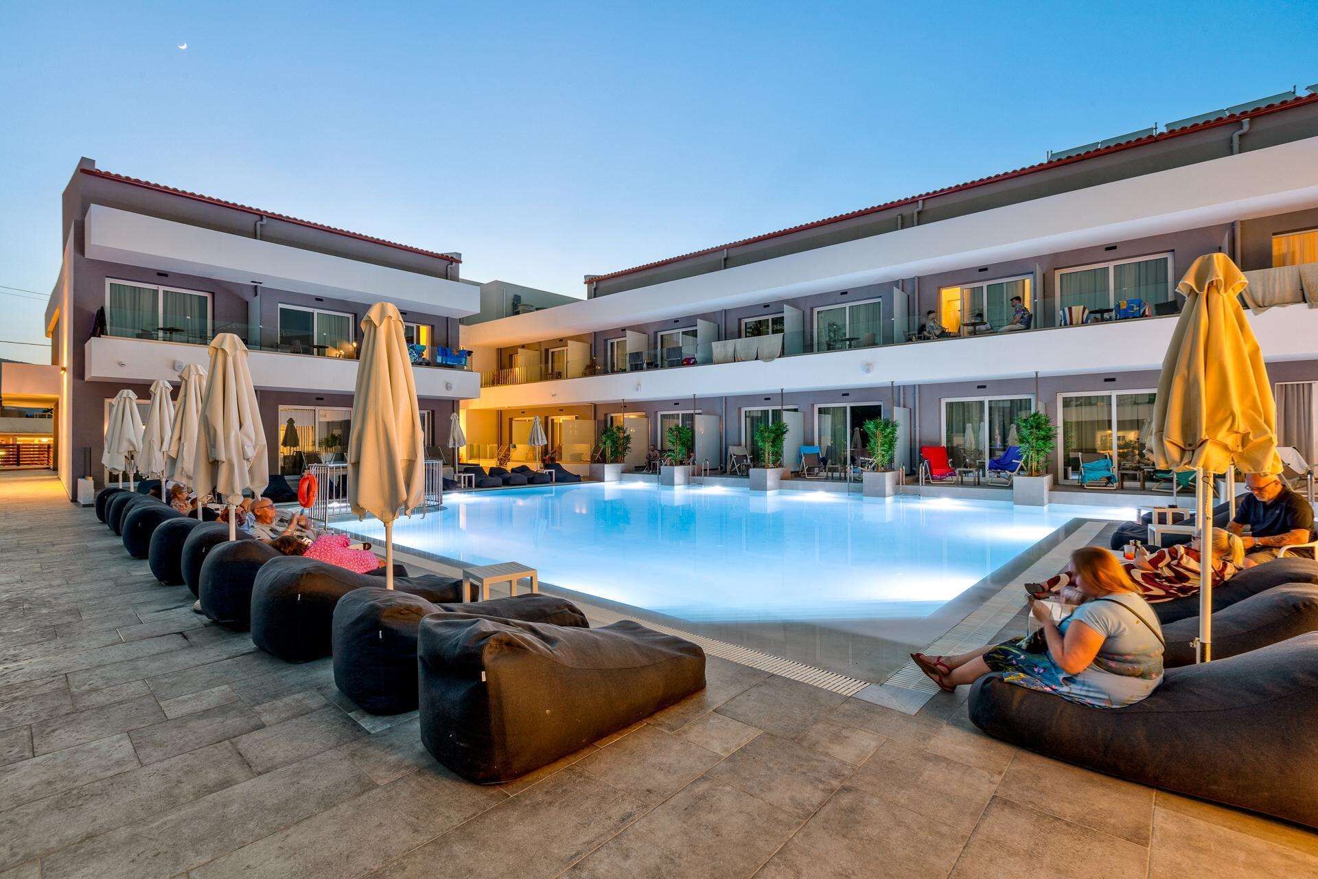 A poolside area with lounge chairs and umbrellas, a pool, and a building with multiple balconies.