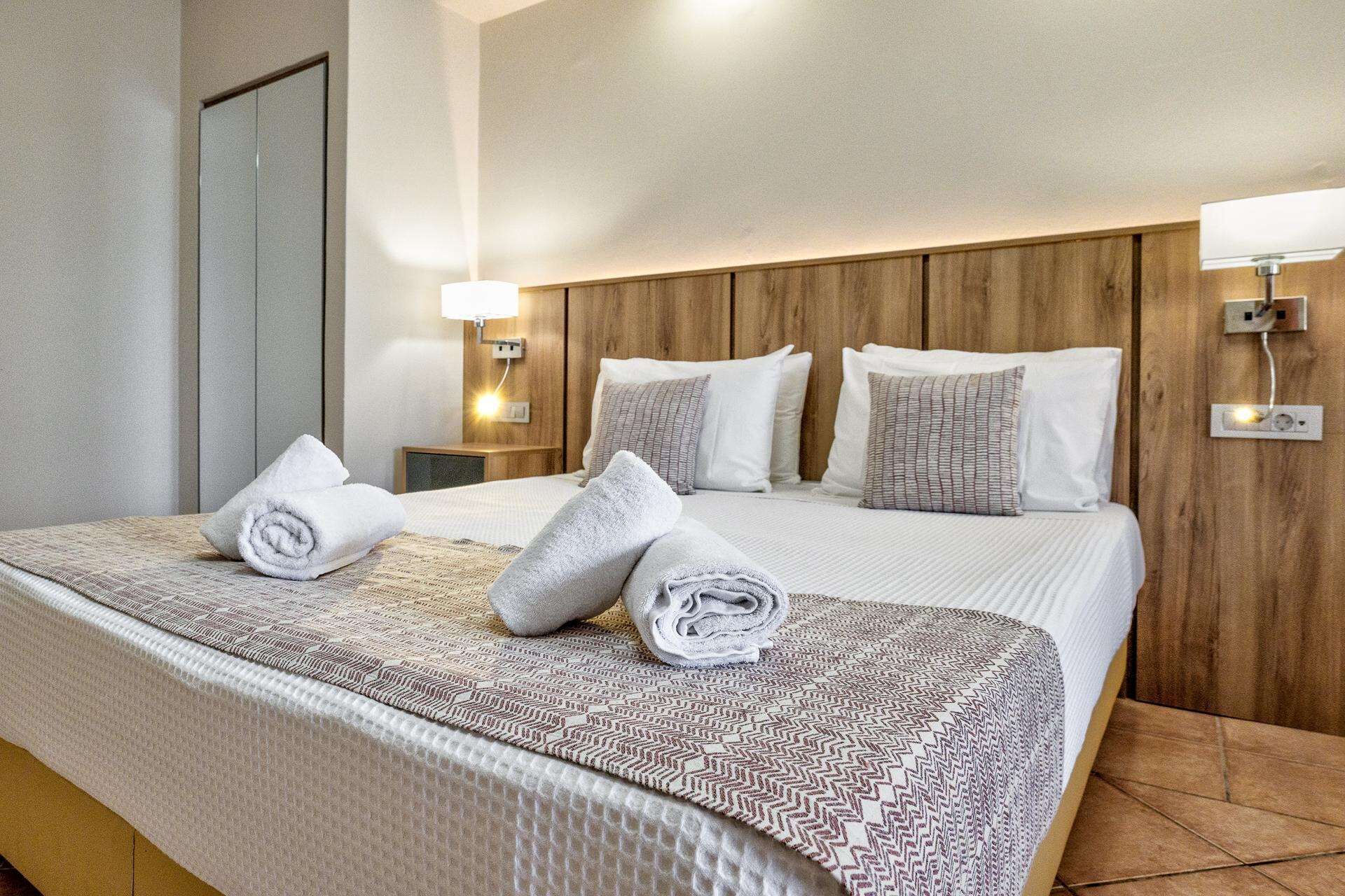 A hotel room with a large bed, two bedside tables, a wooden headboard, and wall-mounted lights.