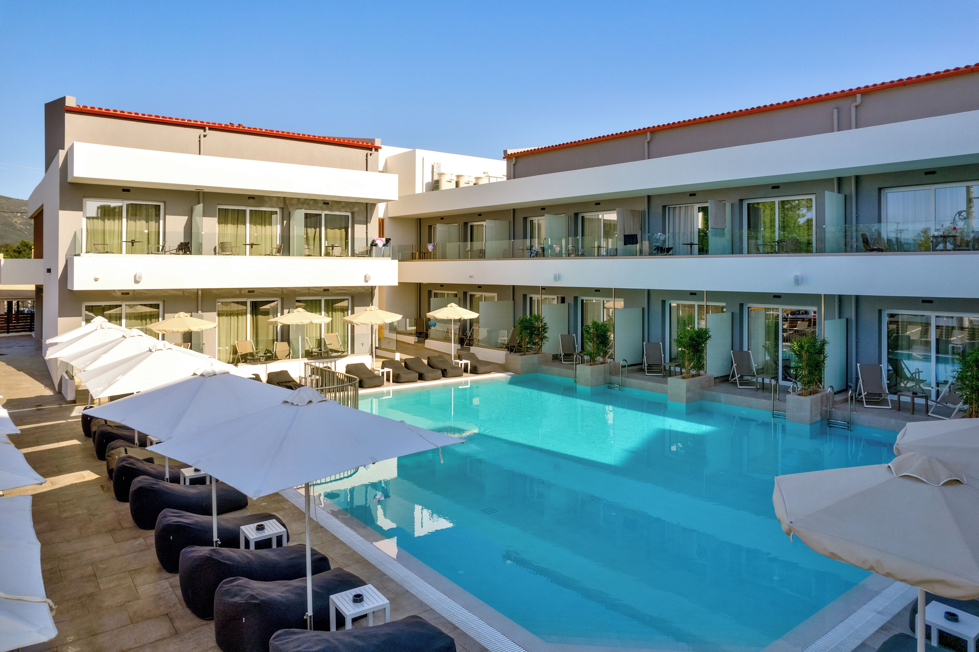 A modern hotel with a large outdoor pool, multiple balconies, and outdoor seating areas.