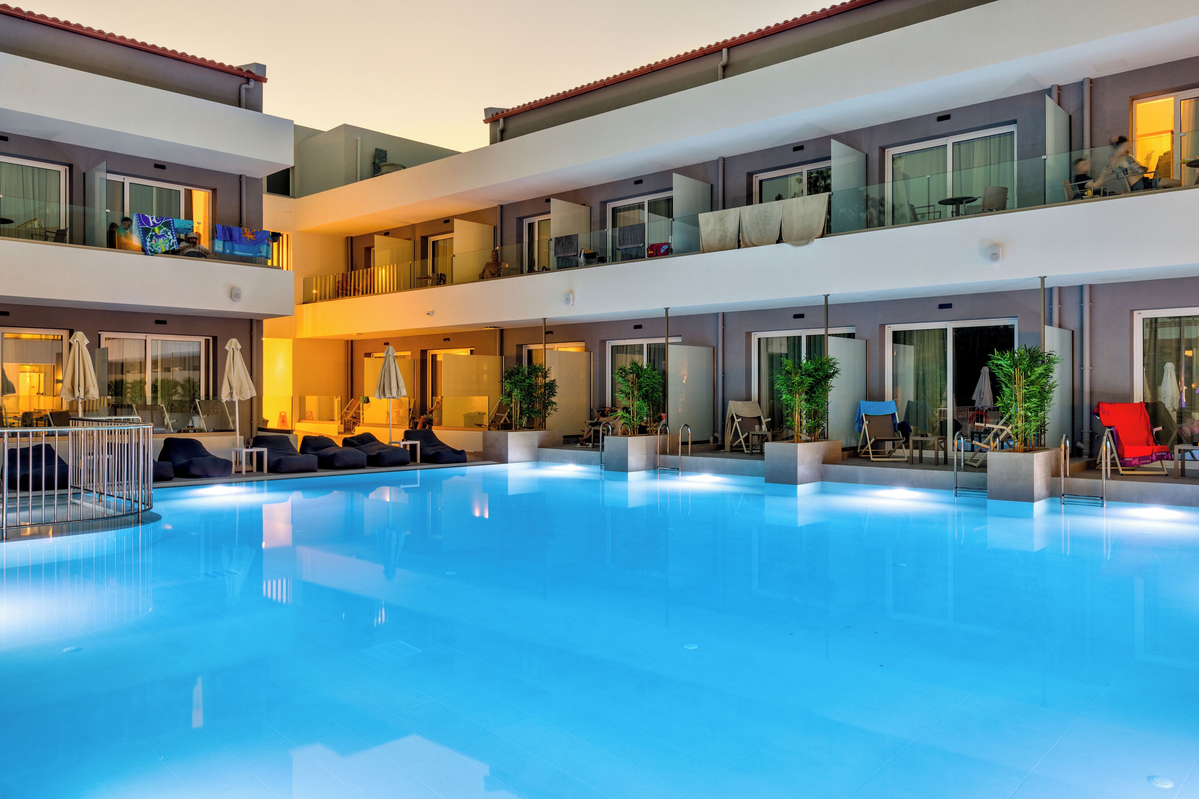 A multi-level hotel with a central swimming pool, balconies with glass railings, and outdoor seating areas.