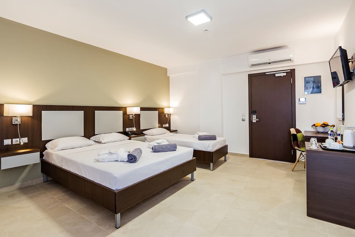 A hotel room with two beds, a desk, a chair, and a TV.