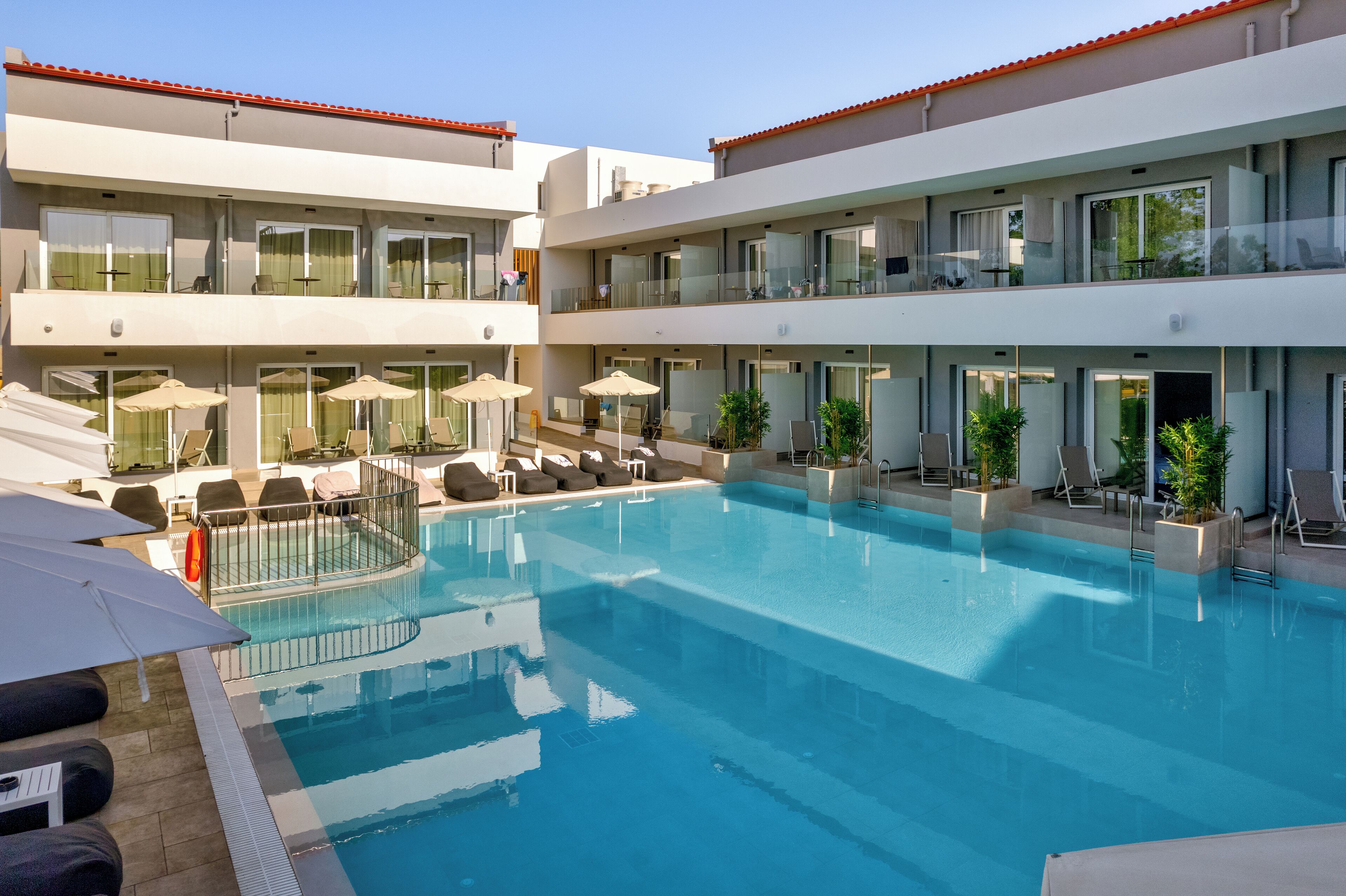 Un hotel moderno con piscina central, varios balcones y zonas de estar al aire libre.