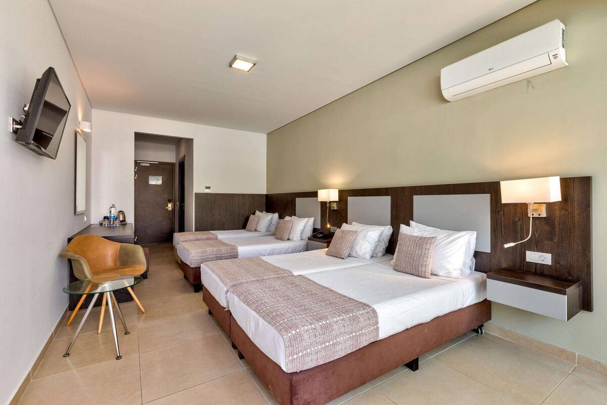 A hotel room with two beds, a desk, a chair, and a TV.