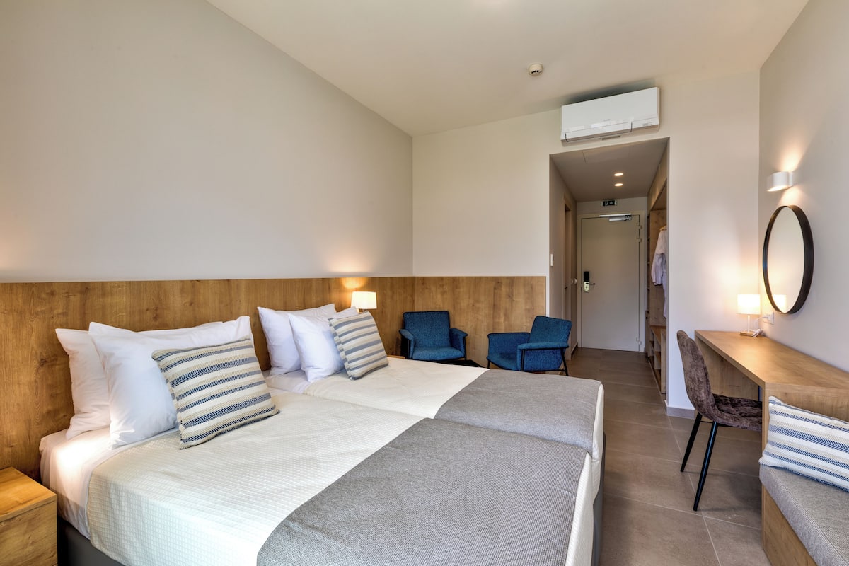 A hotel room with a large bed, two chairs, a desk, and a mirror.