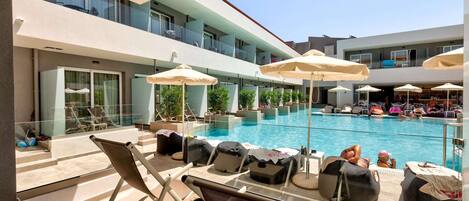 A poolside area with lounge chairs and umbrellas, a clear view of the pool, and a building with multiple balconies.