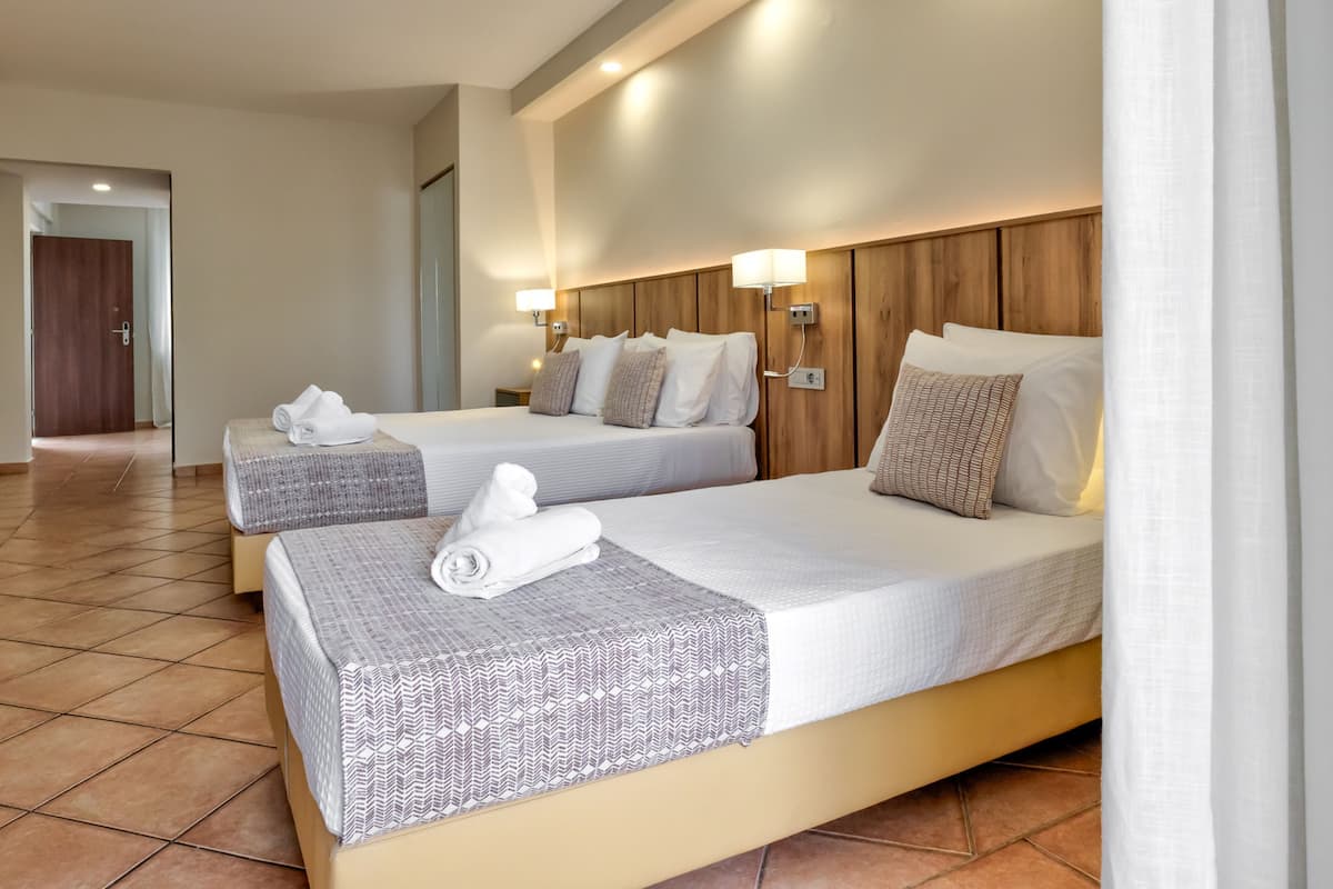 A hotel room with two beds, each with a patterned bedspread, white linens, and a rolled towel on the bed.
