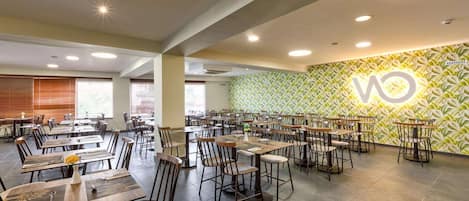 A spacious dining area with multiple tables and chairs, a patterned wall, and ceiling lights.