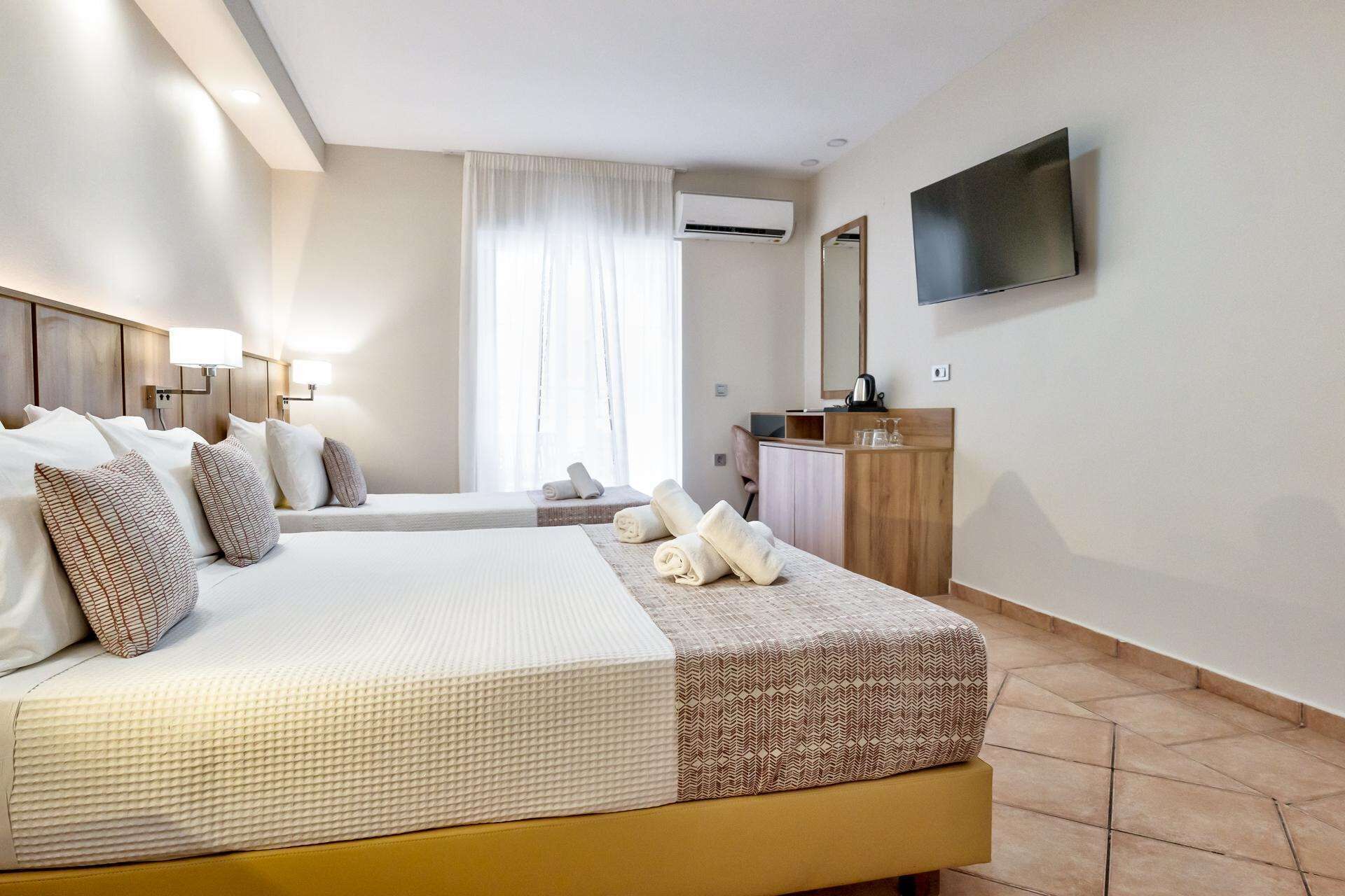 A hotel room with a large bed, a television, a desk, and a window with curtains.