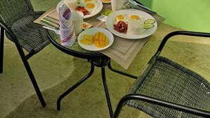 A dining table with plates of food, two chairs, a potted plant, and a window with bars. - Tropical Stay Accommodations (Tagbilaran)