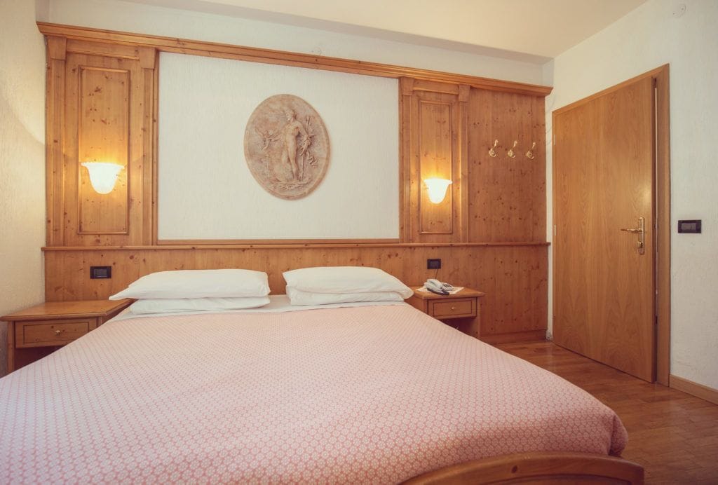 Una camera da letto con un letto grande, una testiera in legno, due comodini, una lampada a parete e una porta.