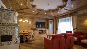 A cozy living room with a wooden ceiling, a TV, red sofas, and a patterned cabinet. - Hotel Centrale (Pejo)