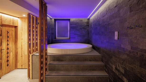 A modern bathroom with a wooden staircase, a bathtub, and a stone wall. - Hotel Centrale (Pejo)
