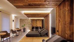 A modern interior with a wooden ceiling, a stone wall, a sofa, and a small table with chairs. - Hotel Centrale (Pejo)
