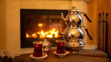 A traditional metal teapot with a wooden handle, accompanied by two glass cups with red liquid, set on a wooden table in front of a fireplace.