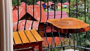A balcony with wooden tables and chairs, overlooking a forested valley with red-roofed buildings. - Ayder Koru Otel (Camlihemsin)