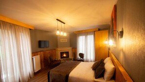 A hotel room with a large bed, a television, a fireplace, and a seating area with a table and chairs. - Ayder Koru Otel (Camlihemsin)