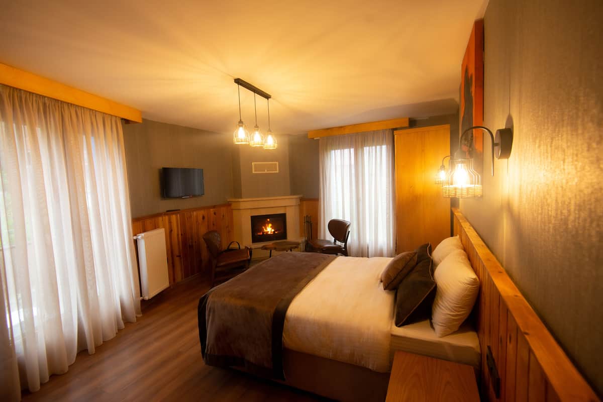 A hotel room with a large bed, a television, a fireplace, and a seating area with a table and chairs.