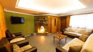 A living room with a fireplace, leather sofas, a TV, and a chess table. - Ayder Koru Otel (Camlihemsin)