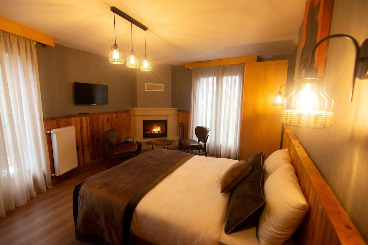 A hotel room with a bed, a television, a fireplace, and a dining area.