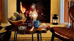 A cozy living room with a fireplace, a table with a bowl of fruit, two mugs, and a leather chair. - Ayder Koru Otel (Camlihemsin)