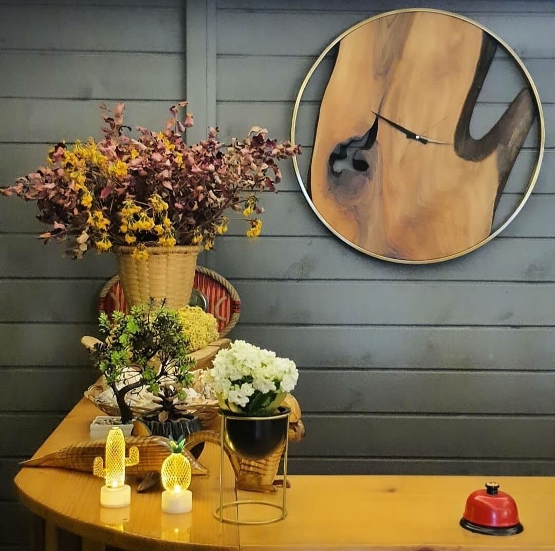 Une table en bois ornée d’une horloge, d’une cloche rouge et de divers objets décoratifs, notamment un panier de fleurs et un petit cactus.