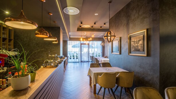 Un interior de restaurante moderno con suelo de madera, iluminación colgante y cuadros en las paredes.