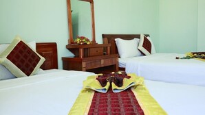 A hotel room with two beds, a wooden dresser, a mirror, and a floral arrangement on the dresser. - A Dong Hotel (Da Nang)